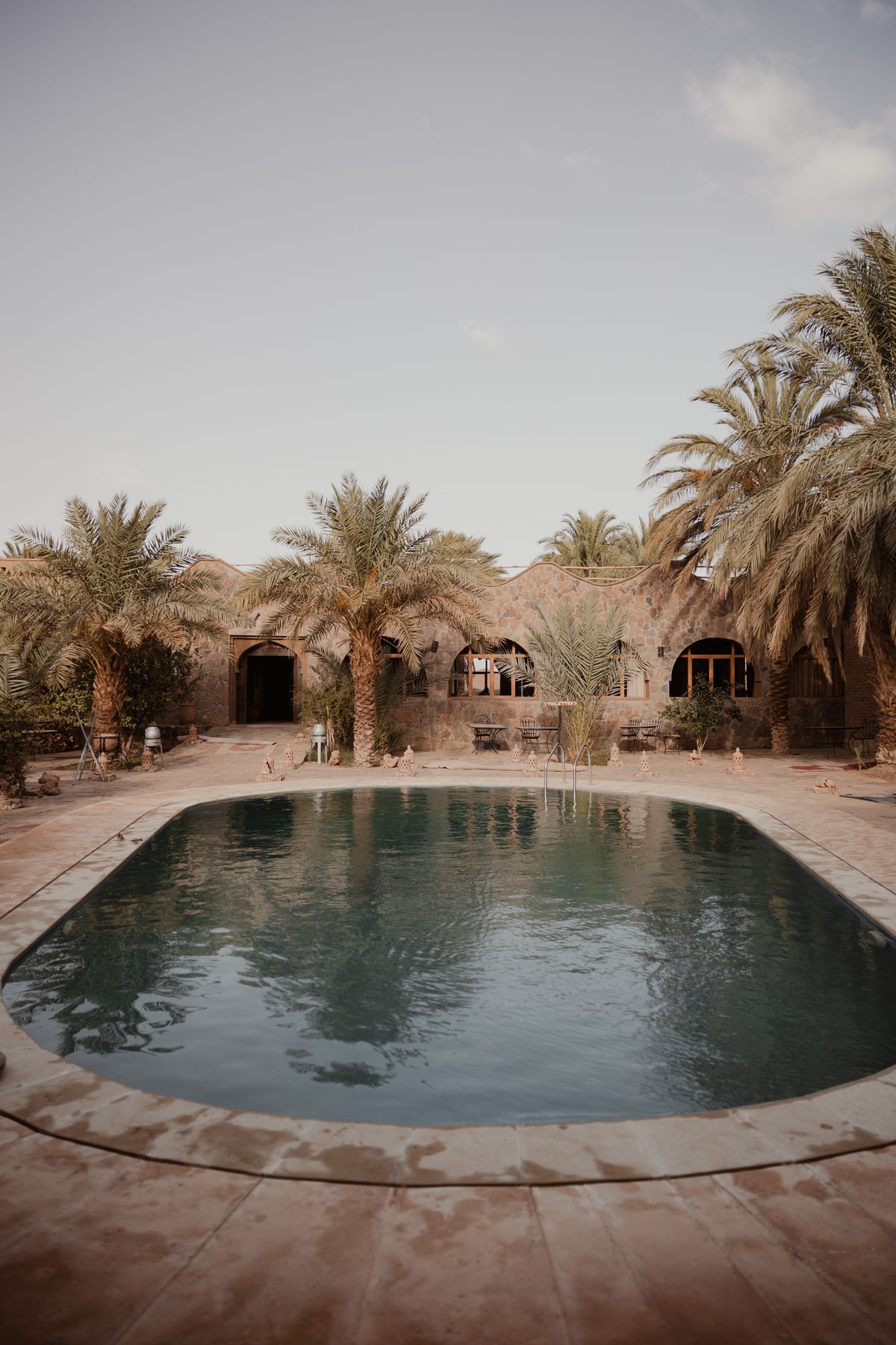 Sunlit resort pool surrounded by palms and warm architecture
